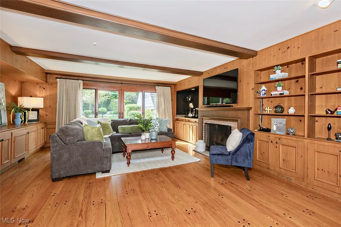 Library/family room featuring wood walls, beam ceiling, light wood-style flooring, and a fireplace