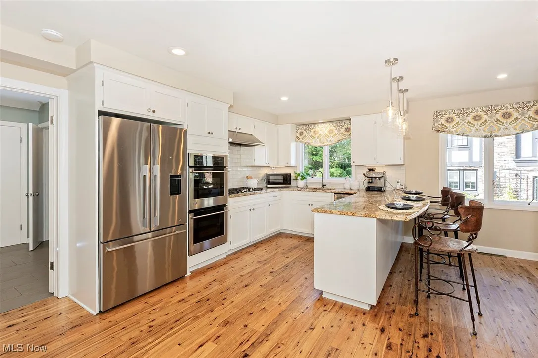 Kitchen featuring stainless steel appliances, a peninsula, light wood-style floors, a breakfast bar, and tasteful backsplash