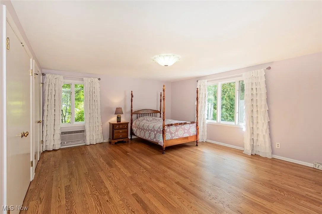 Bedroom with light wood finished floors, multiple windows, and a wall unit AC