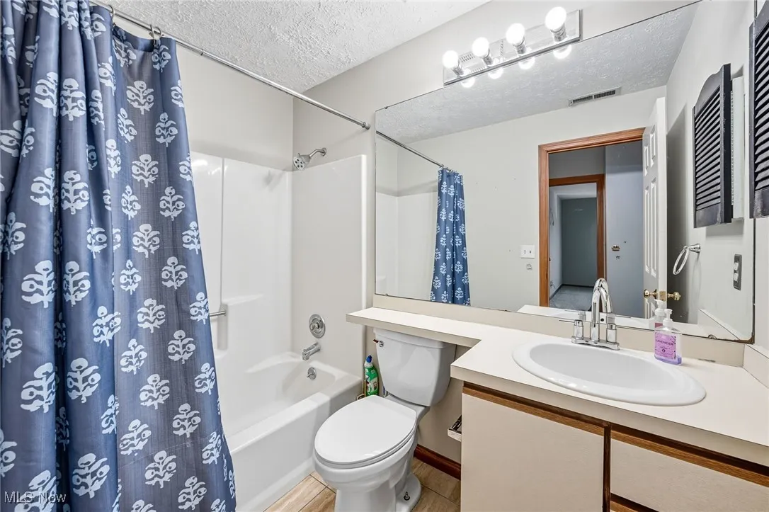 Bathroom featuring shower / bath combination with curtain, a textured ceiling, and vanity