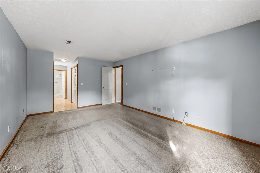 Unfurnished bedroom featuring light carpet, a textured ceiling, ensuite bathroom, and a closet