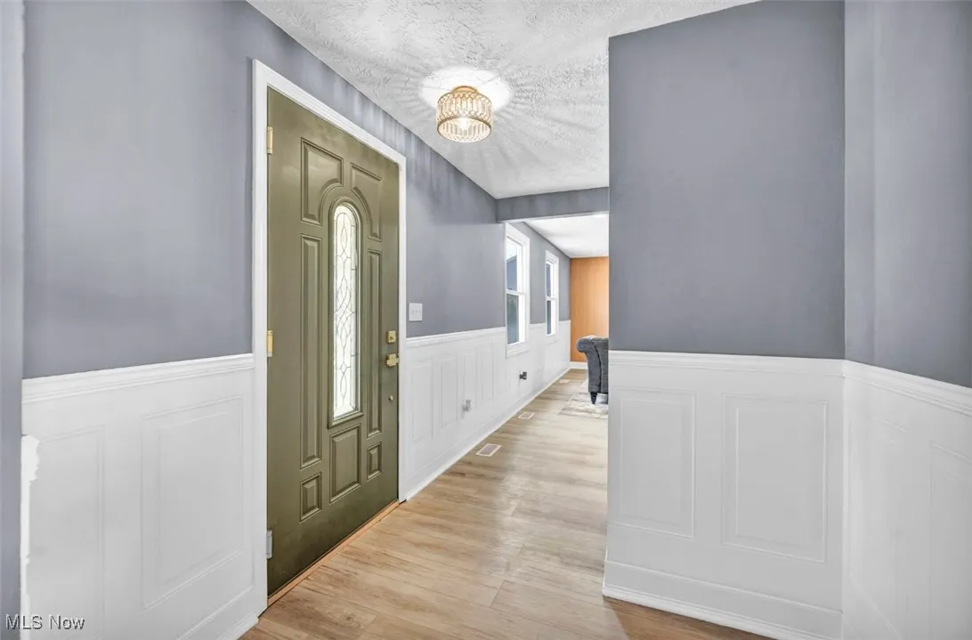 Entryway with wainscoting, a decorative wall, a textured ceiling, light wood-type flooring, and a chandelier