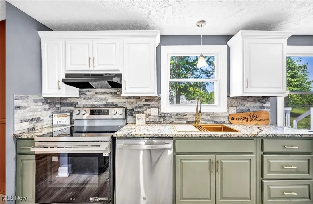 Kitchen with green cabinets, appliances with stainless steel finishes, white cabinetry, tasteful backsplash, and a textured ceiling