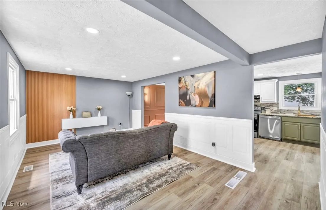 Living area with a textured ceiling, light wood finished floors, recessed lighting, a wainscoted wall, and beamed ceiling