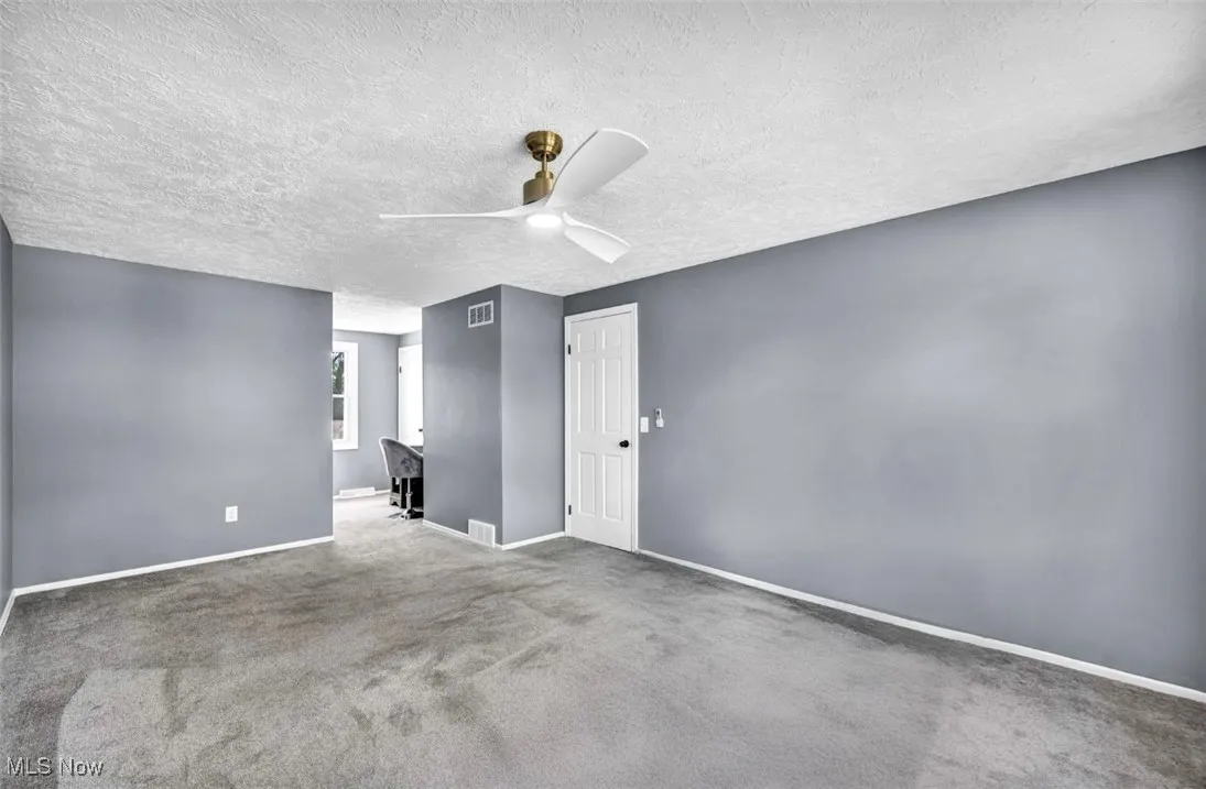 Empty room featuring a ceiling fan, a textured ceiling, and carpet flooring