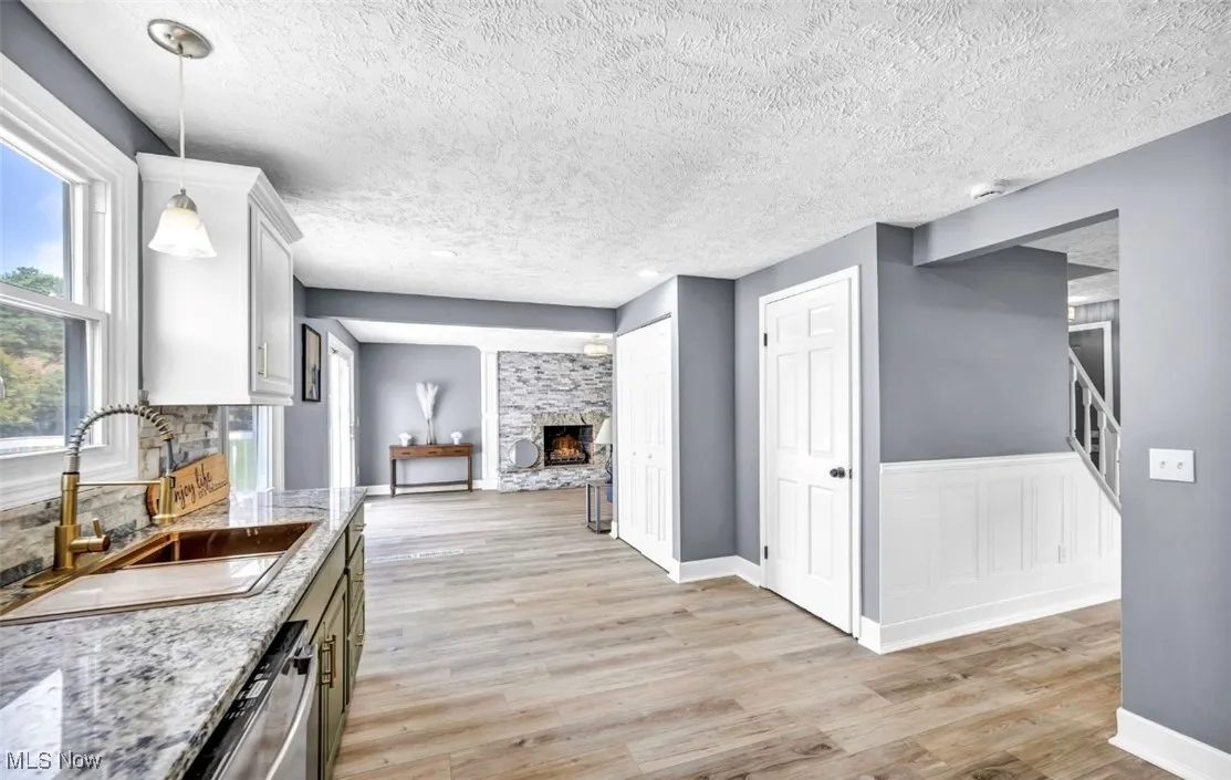 Kitchen with light stone counters, light wood-type flooring, a textured ceiling, a fireplace, and stainless steel dishwasher