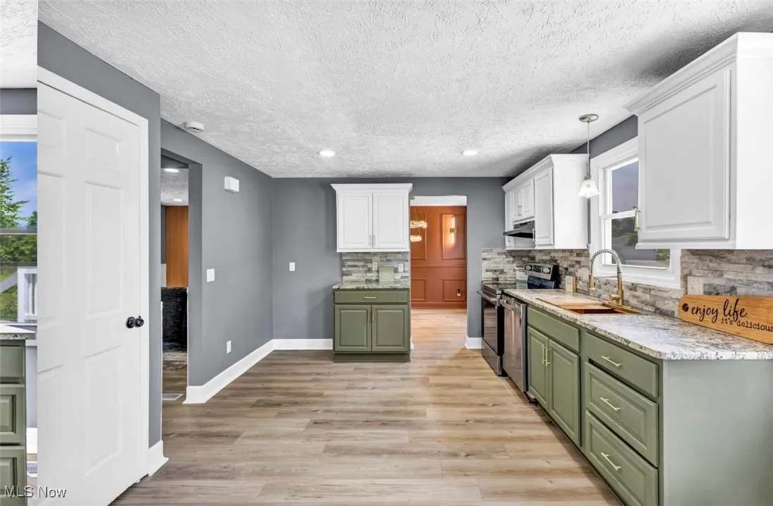 Kitchen featuring green cabinetry, white cabinetry, stainless steel appliances, light wood-type flooring, and a textured ceiling