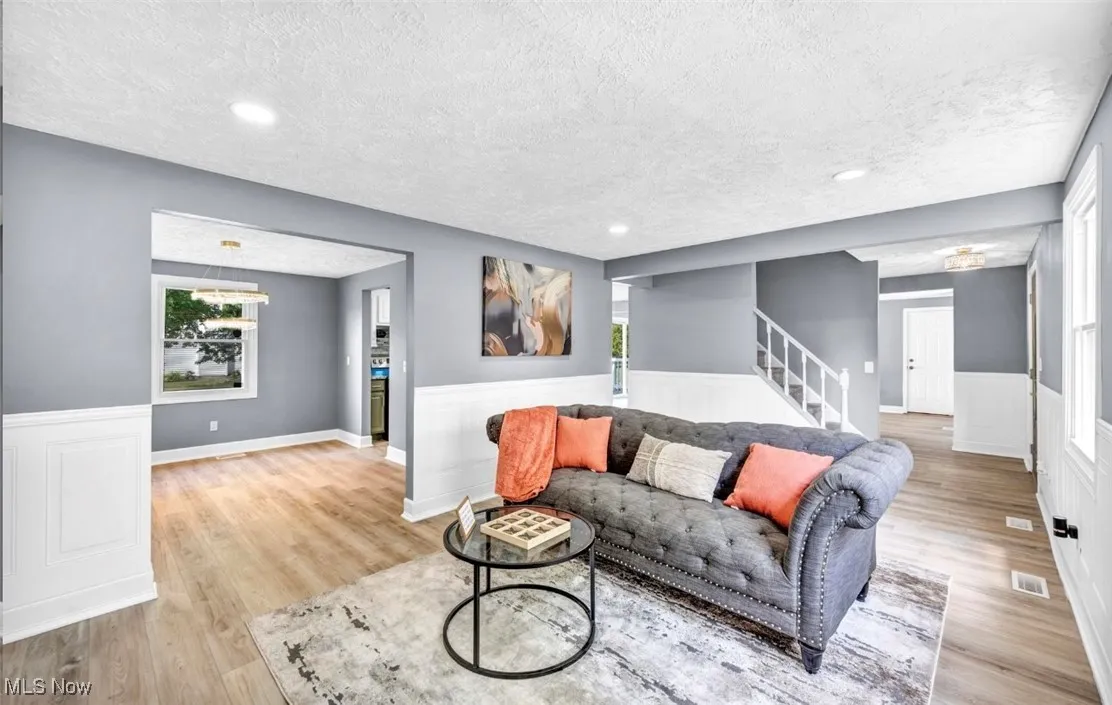 Living area with light wood-type flooring, a textured ceiling, recessed lighting, stairway, and wainscoting