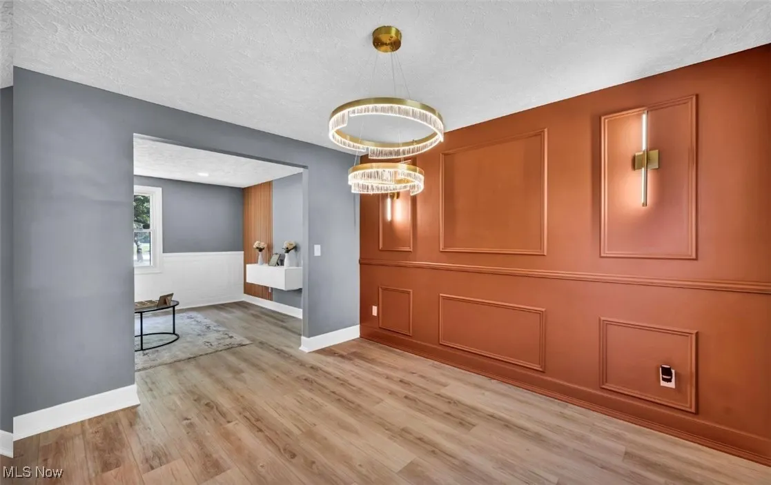 Unfurnished dining area with light wood-style floors, a textured ceiling, a wainscoted wall, a decorative wall, and a chandelier