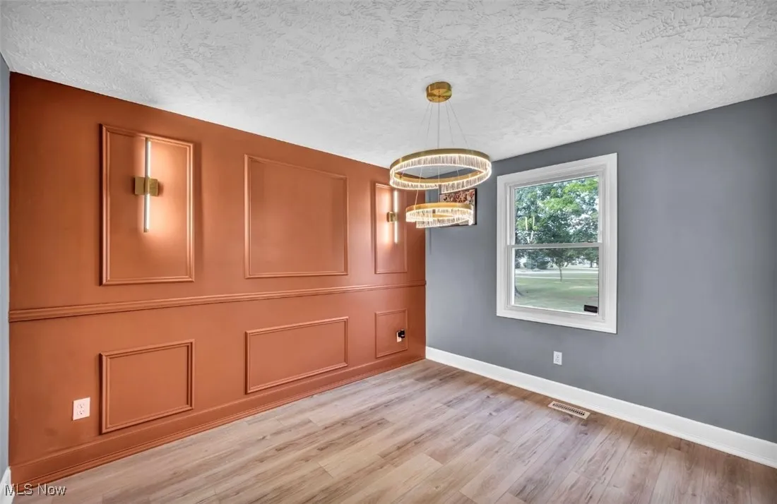 Unfurnished dining area with light wood-style floors, a textured ceiling, and a chandelier