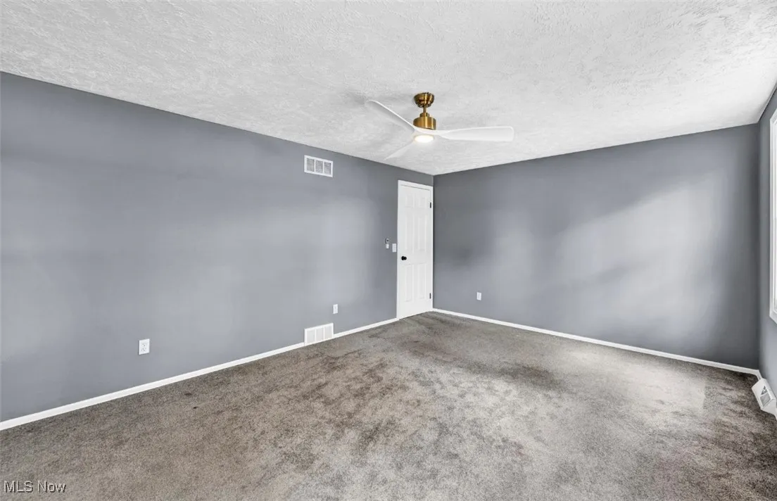 Empty room with a textured ceiling, carpet floors, and ceiling fan