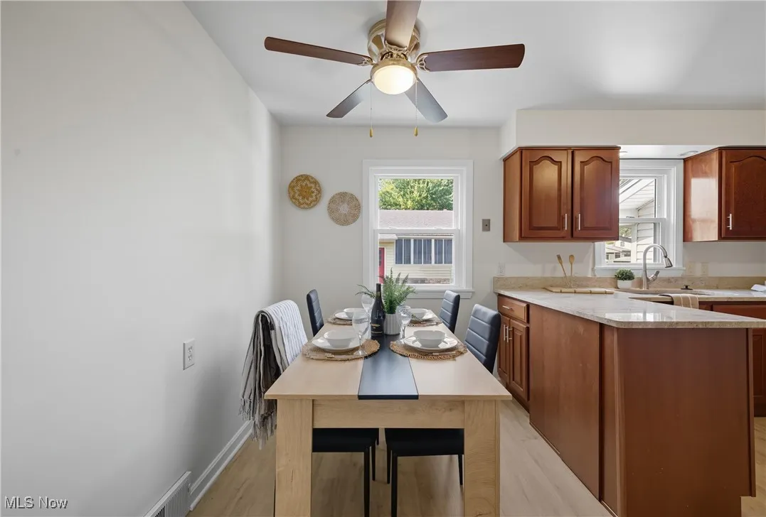 Kitchen with light wood-style floors, light stone countertops, brown cabinetry, a peninsula, and a ceiling fan