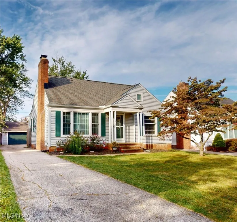 View of front facade with a chimney, a front lawn, an outbuilding, a shingled roof, and a garage
