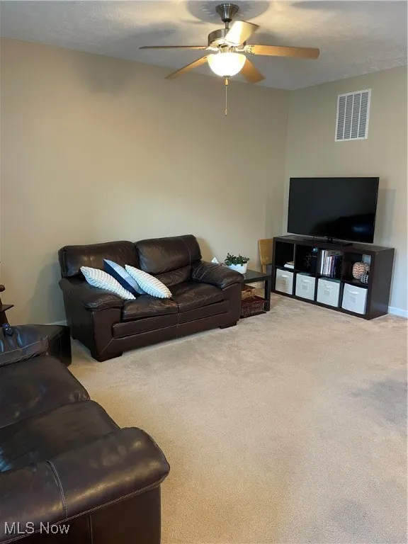 Living area featuring light colored carpet, a textured ceiling, and a ceiling fan