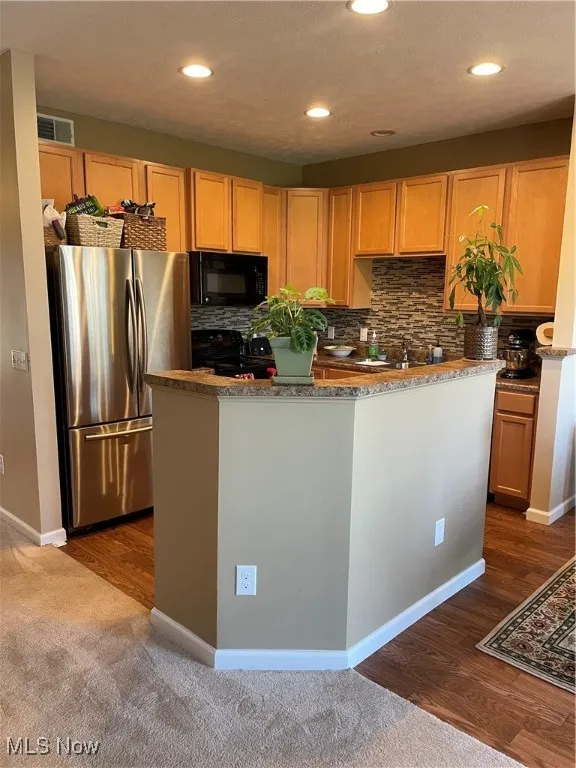 Kitchen featuring fridge, stainless steel microwave, stove, dark wood-type flooring, and a kitchen island