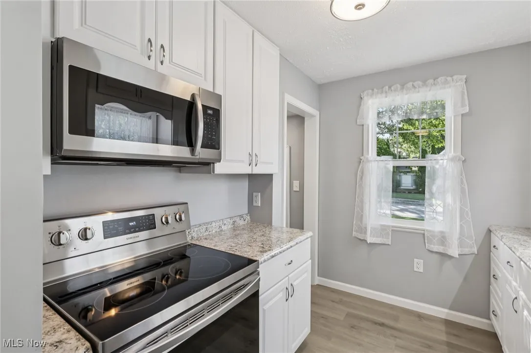 Kitchen featuring appliances with stainless steel finishes, white cabinets, light wood finished floors, light stone countertops, and a textured ceiling
