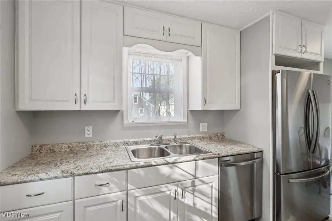 Kitchen featuring appliances with stainless steel finishes, white cabinets, and light stone counters