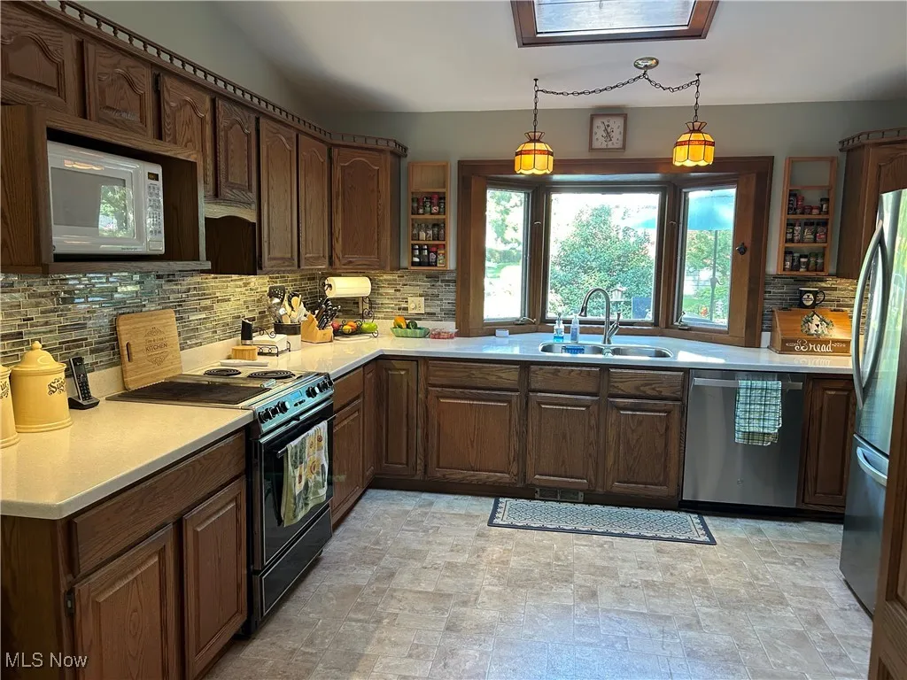 Kitchen with stainless steel appliances, open shelves, a skylight, light countertops, and decorative backsplash