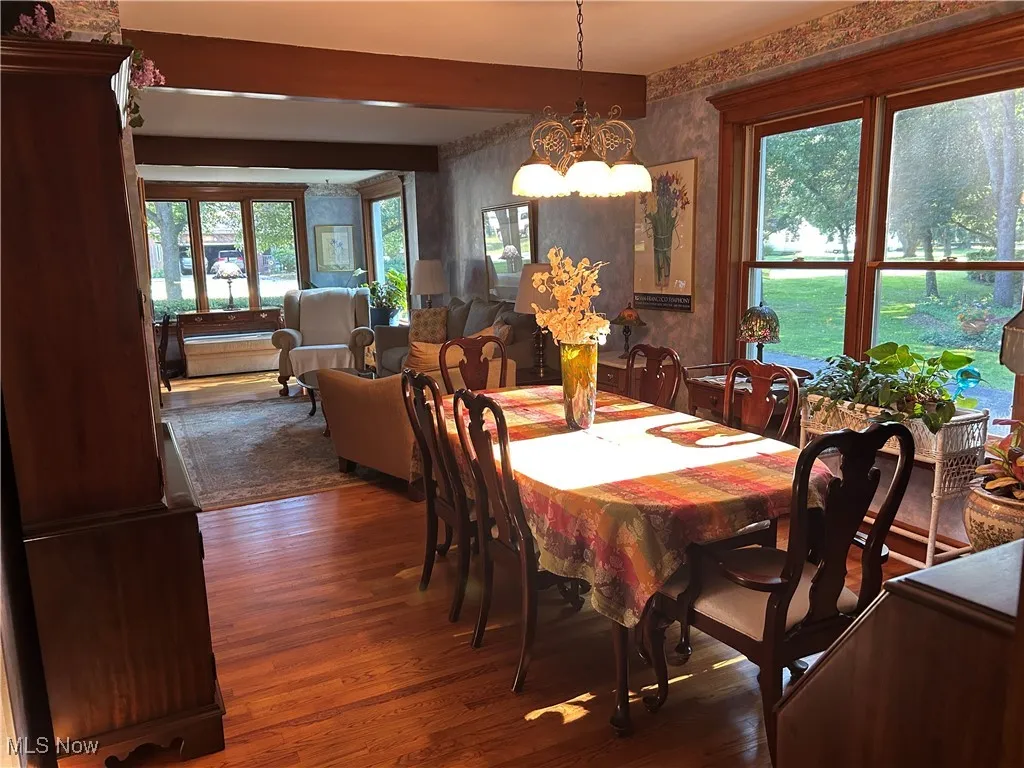 Dining area with wallpapered walls, a chandelier, wood finished floors, and beamed ceiling