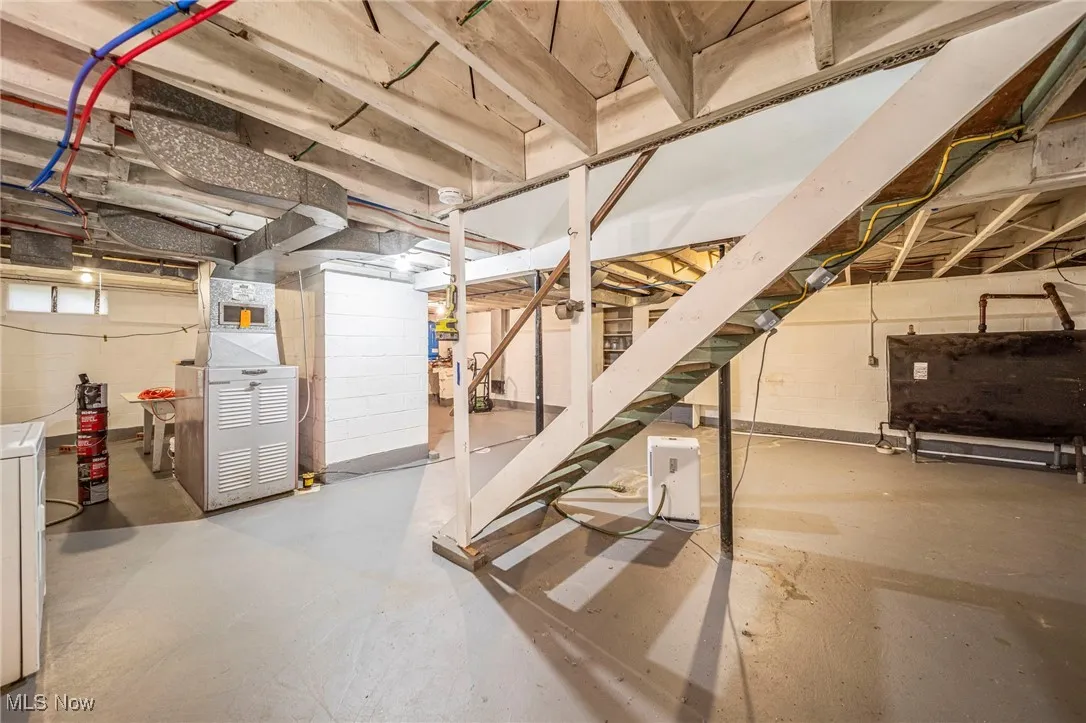 Unfinished basement featuring oil tank, stairs, heating unit, and washer / clothes dryer