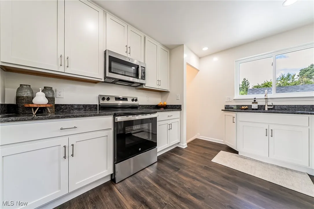 Kitchen featuring stainless steel appliances, white cabinetry, dark stone counters, and recessed lighting