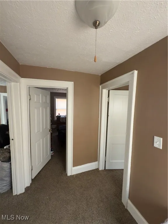 Unfurnished bedroom featuring a textured ceiling and dark carpet
