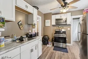 Kitchen featuring appliances with stainless steel finishes, white cabinetry, light countertops, light wood-style floors, and a ceiling fan