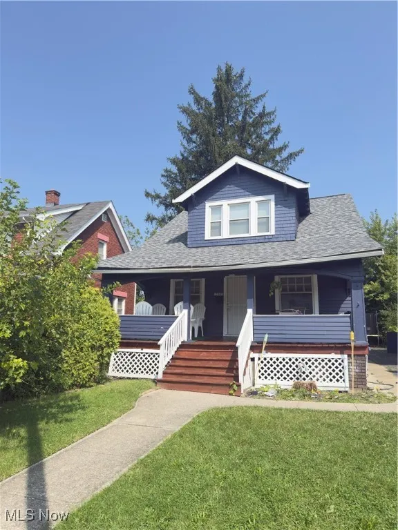 Bungalow-style house with covered porch, a shingled roof, and a front lawn