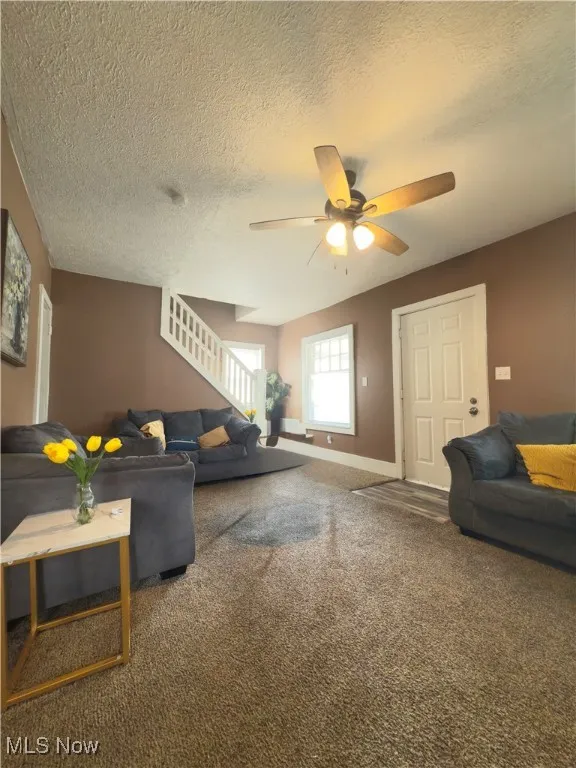 Carpeted living area with a textured ceiling, stairs, and ceiling fan