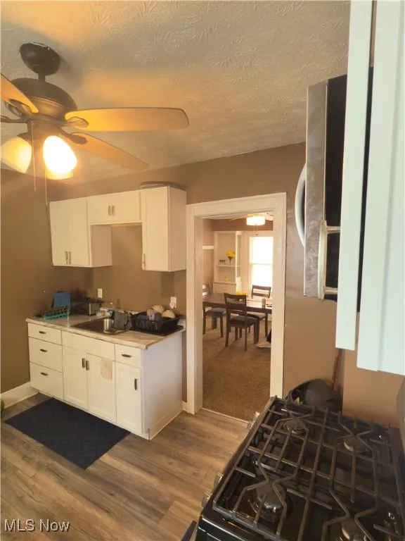 Kitchen featuring white cabinets, gas stove, a textured ceiling, dark wood-type flooring, and light countertops
