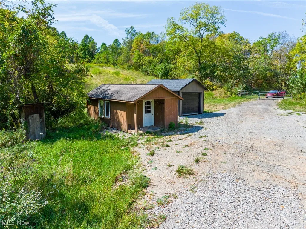 View of front of home featuring an outdoor structure, roof with shingles, a garage, driveway, and a forest view