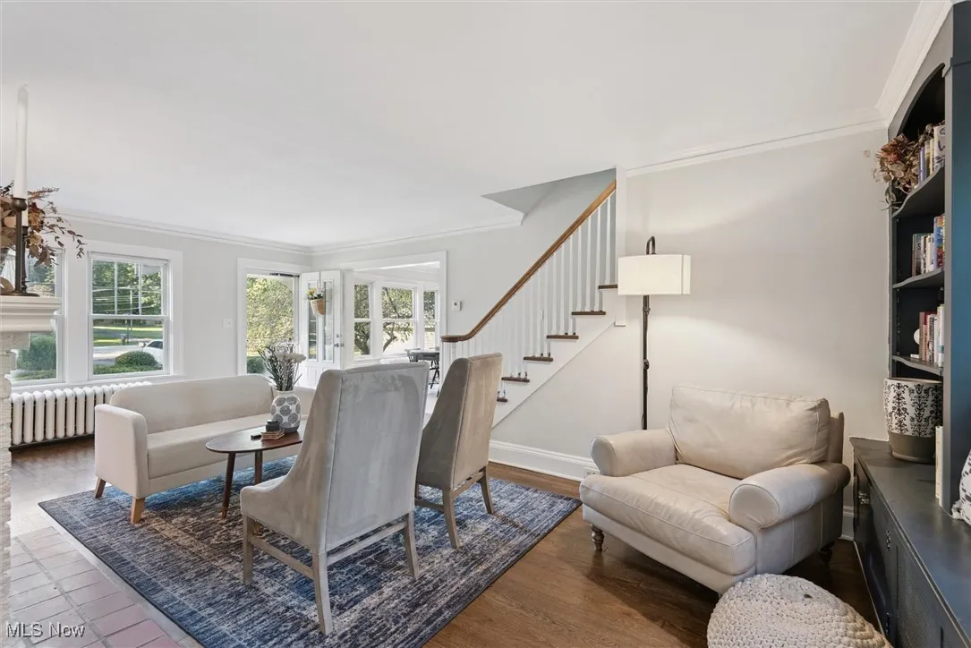 Living area with ornamental molding, wood finished floors, stairway, and radiator heating unit