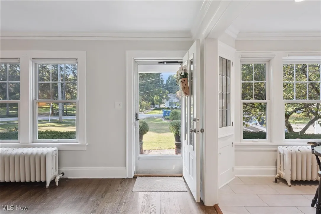 Doorway to outside with radiator, crown molding, healthy amount of natural light, and wood finished floors