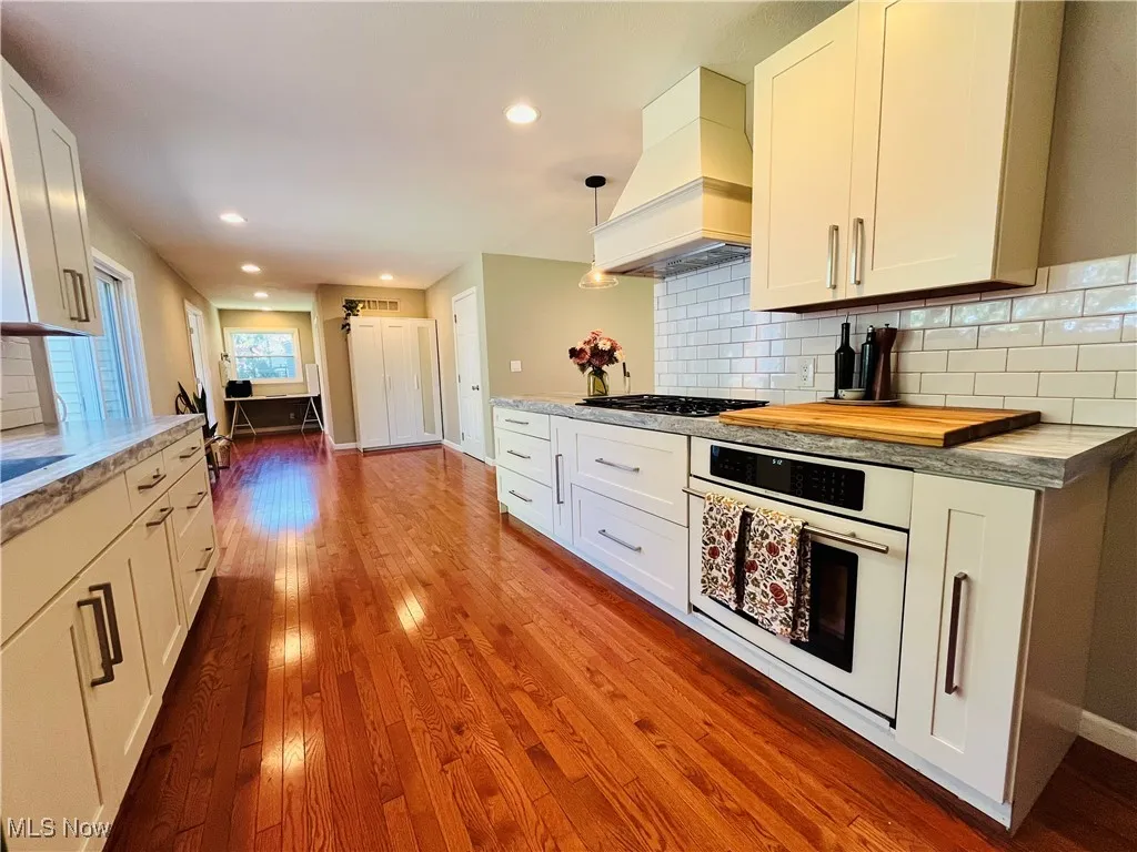 Kitchen featuring backsplash, white oven, custom exhaust hood, white cabinetry, and recessed lighting