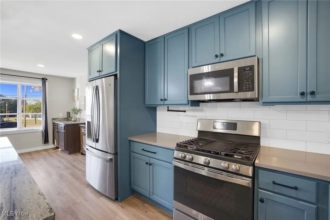 Kitchen with appliances with stainless steel finishes, backsplash, light wood-type flooring, light stone counters, and recessed lighting