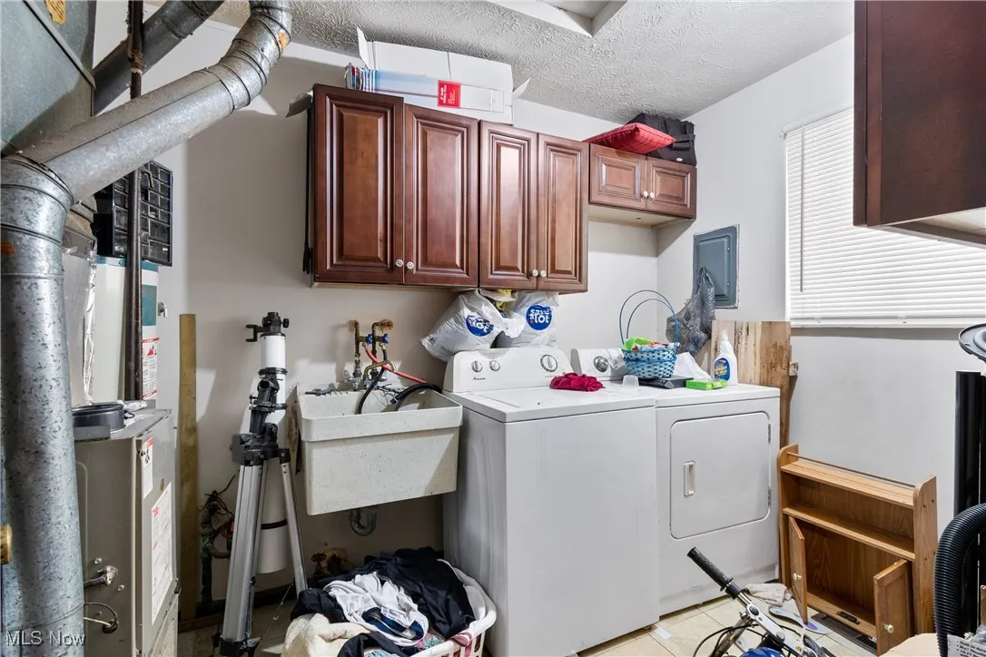 Laundry area with a textured ceiling, washing machine and clothes dryer, light tile patterned floors, cabinet space, and heating unit