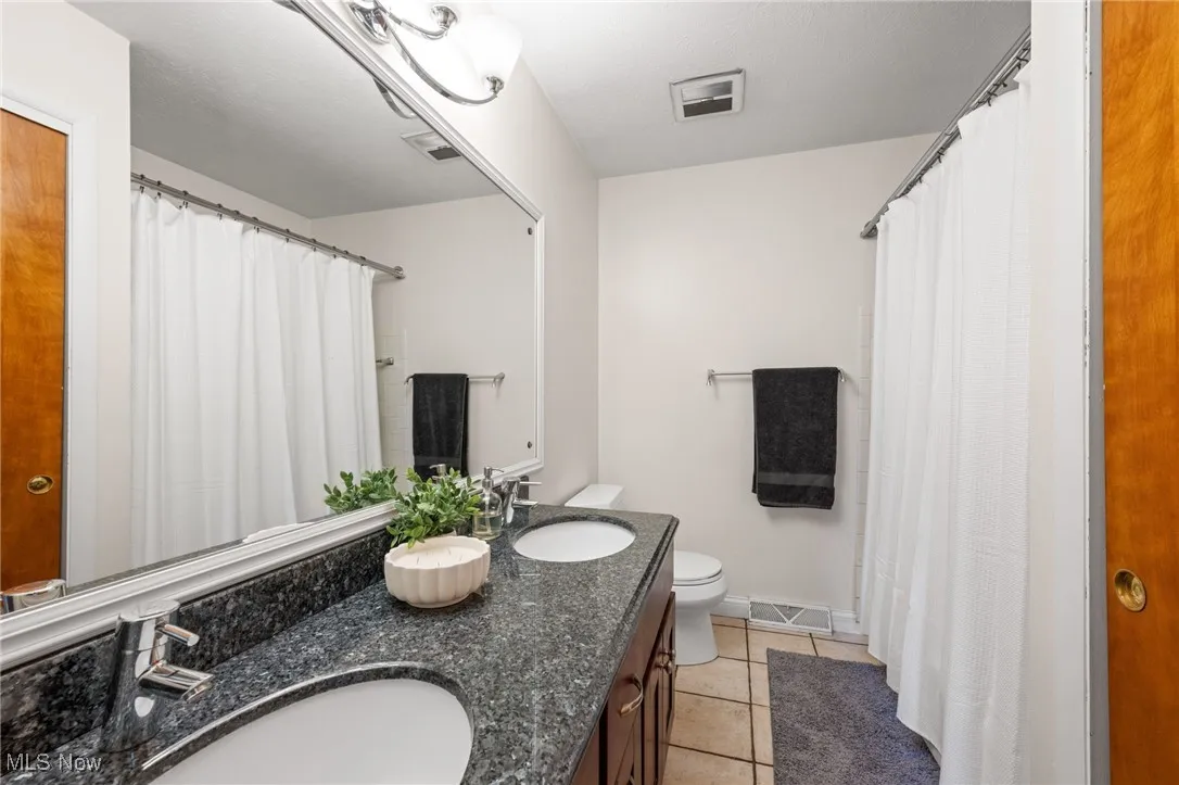 Full bathroom featuring light tile patterned floors, double vanity, and curtained shower
