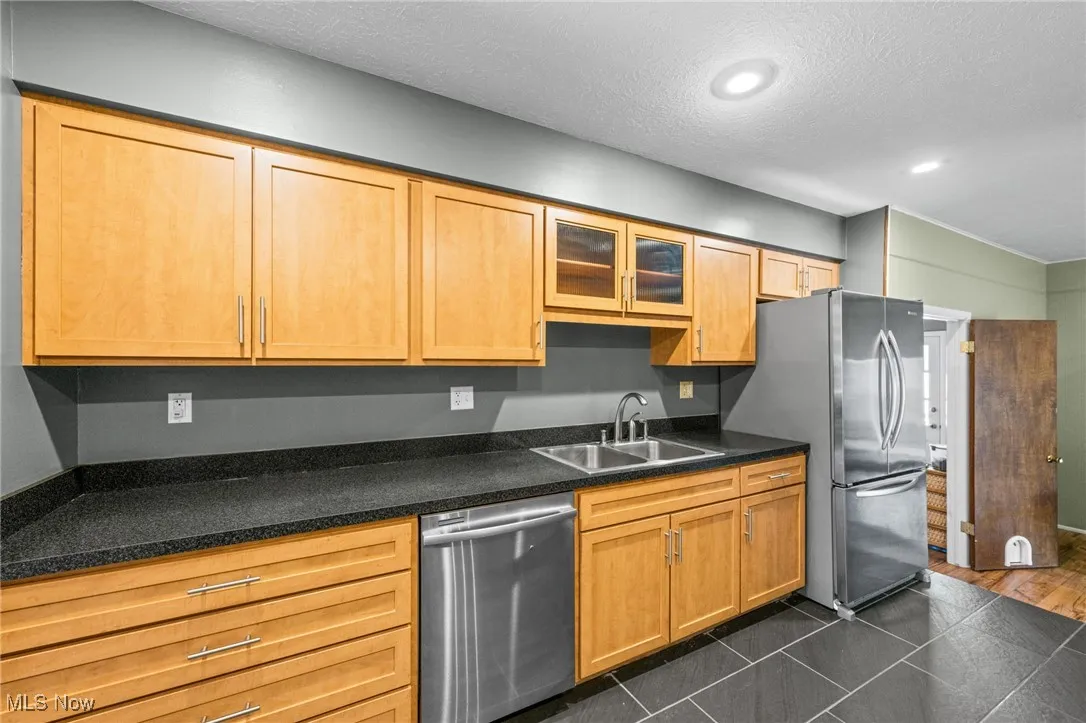 Kitchen with appliances with stainless steel finishes, glass insert cabinets, dark tile patterned flooring, a textured ceiling, and recessed lighting