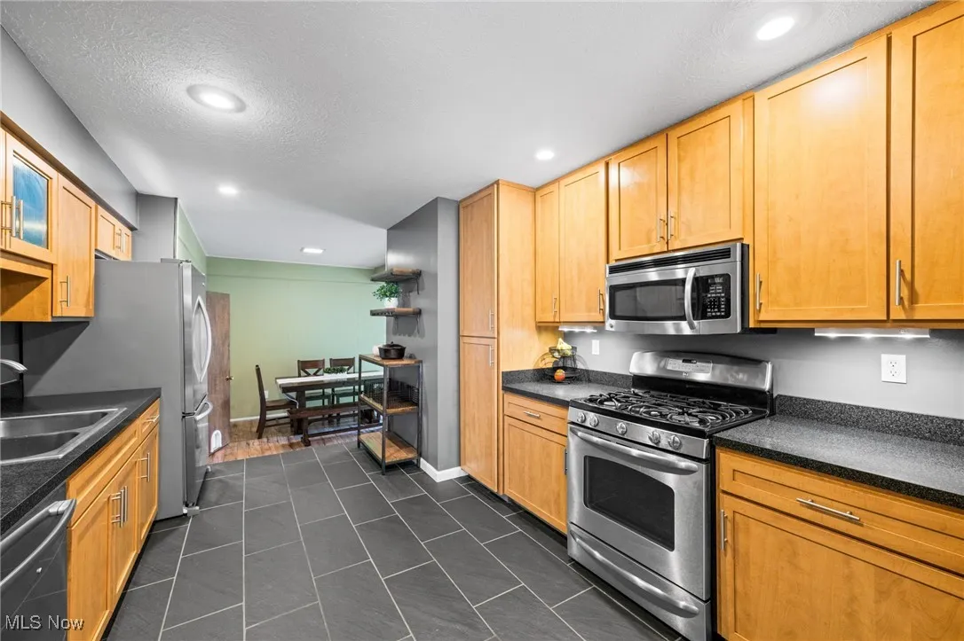 Kitchen featuring appliances with stainless steel finishes, dark tile patterned floors, a textured ceiling, recessed lighting, and dark stone countertops