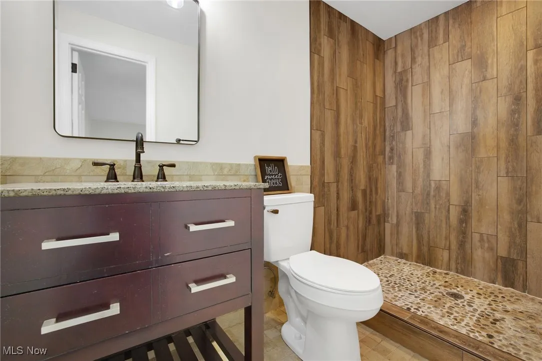 Full bathroom featuring vanity, a stall shower, tile walls, and light tile patterned flooring