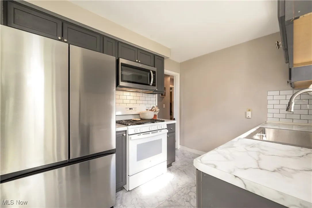 Kitchen with stainless steel appliances, decorative backsplash, light countertops, light marble finish flooring, and gray cabinetry
