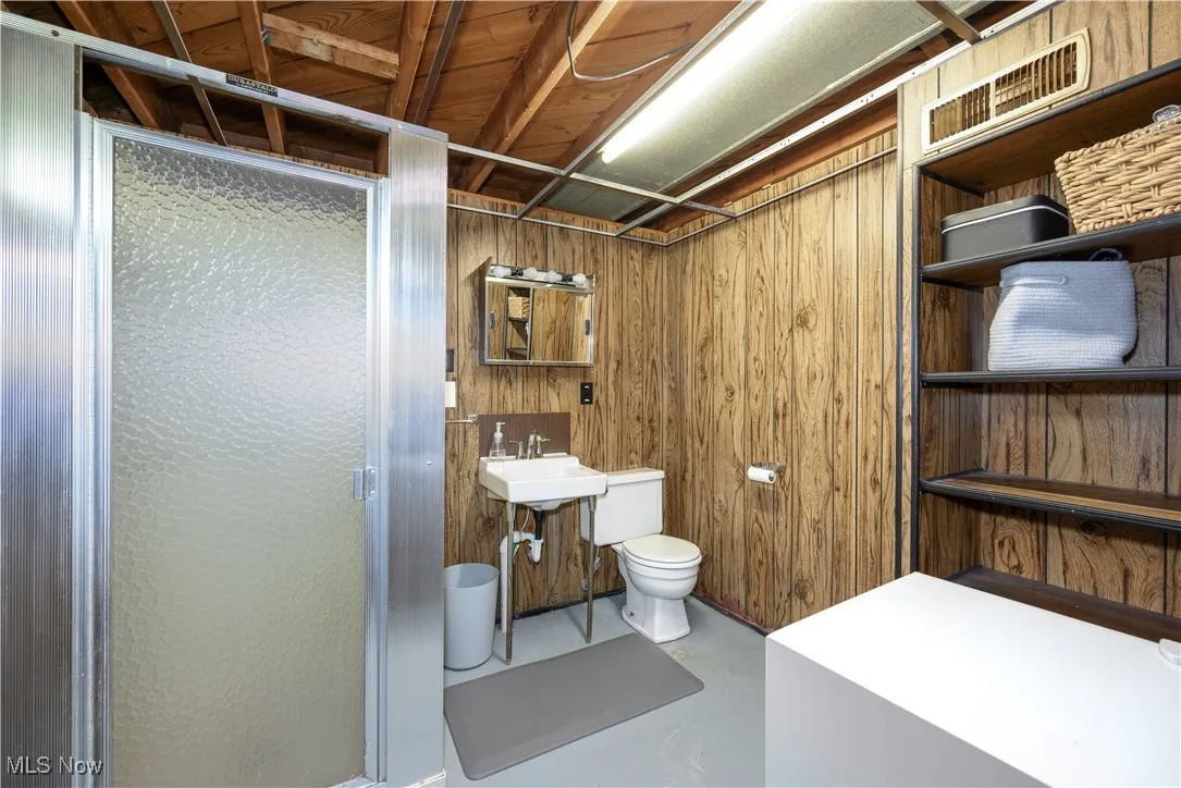 Full bath featuring finished concrete floors, a shower stall, and wood walls