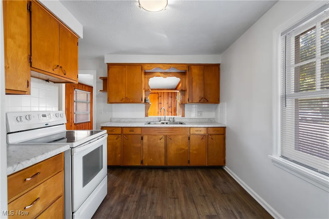 Kitchen featuring white electric stove, light countertops, dark wood-style floors, brown cabinets, and tasteful backsplash