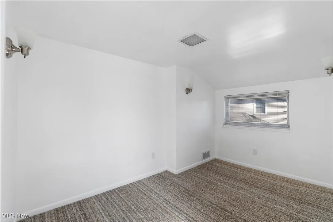 Spare room featuring carpet flooring and vaulted ceiling