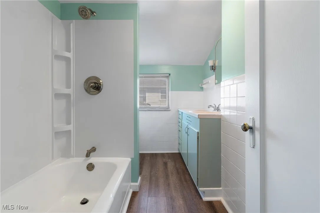 Bathroom featuring dark wood-style flooring, shower / bath combination, vanity, wainscoting, and tile walls