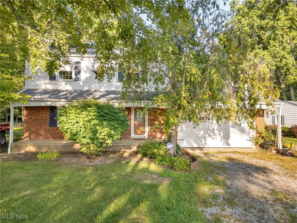 View of property hidden behind natural elements with brick siding, a garage, driveway, and a front lawn
