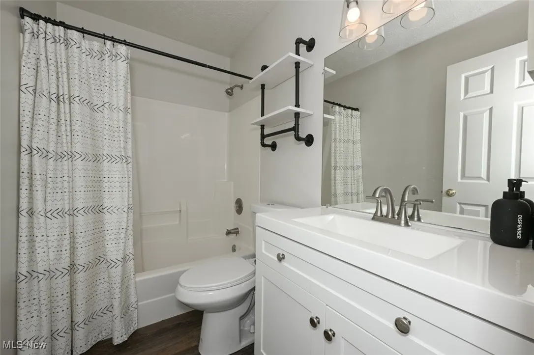 Full bathroom featuring shower / tub combo with curtain, vanity, LVP flooring, and a textured ceiling
