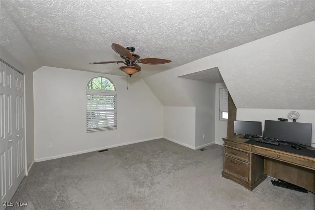 Bedroom with natural light, lofted ceiling, a textured ceiling, light colored carpet, and a ceiling fan