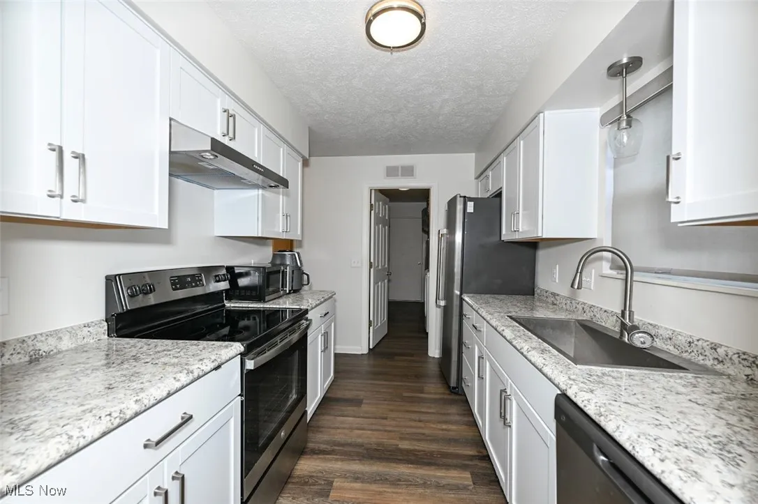 Kitchen with stainless steel appliances, LVP floors, under cabinet range hood, a textured ceiling, and white cabinets