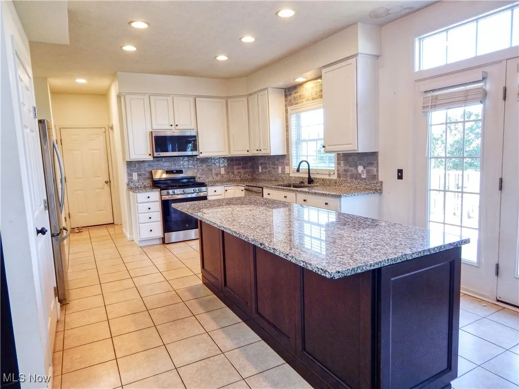 Kitchen featuring backsplash, appliances with stainless steel finishes, light stone counters, white cabinets, and recessed lighting
